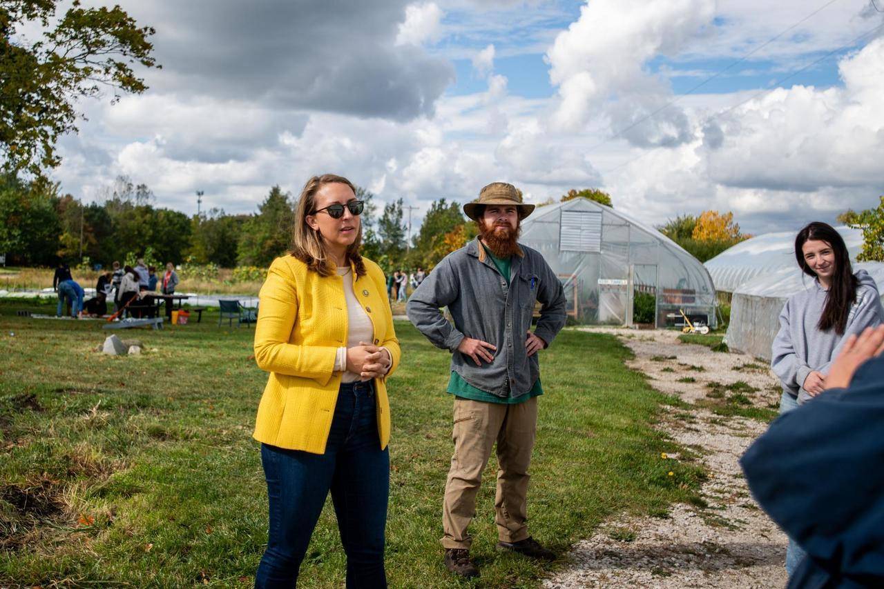 woman in yellow blazer and man in khaki pants and hat talking with students